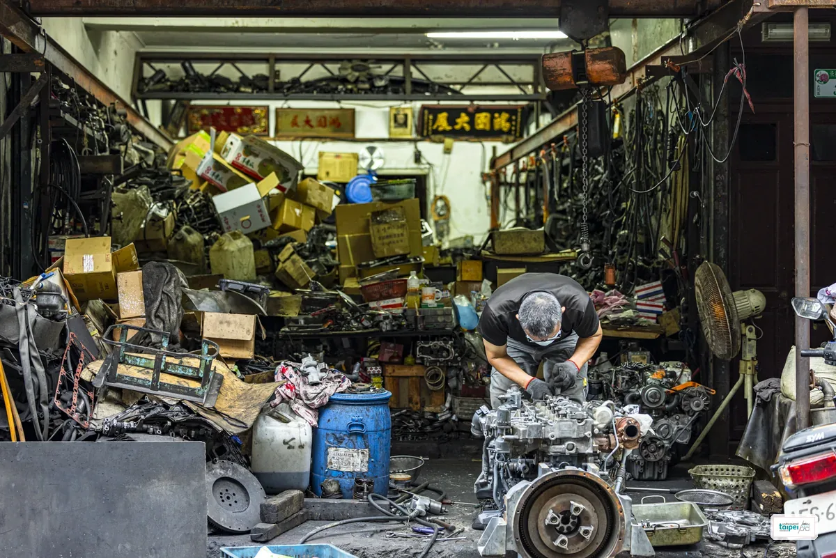 A working auto-parts and repair garage on Chifeng Street, a man bent over a car engine surrounded by stacked parts