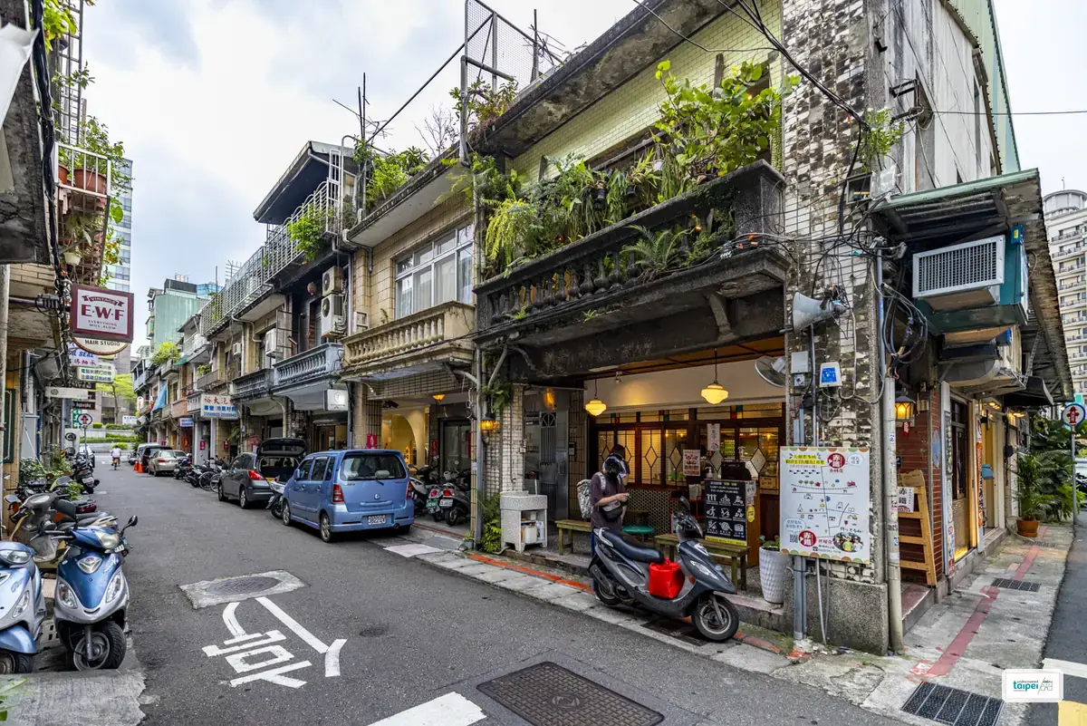 A quiet Chifeng Street lane lined with old tiled shophouses, one draped in balcony greenery above a small eatery