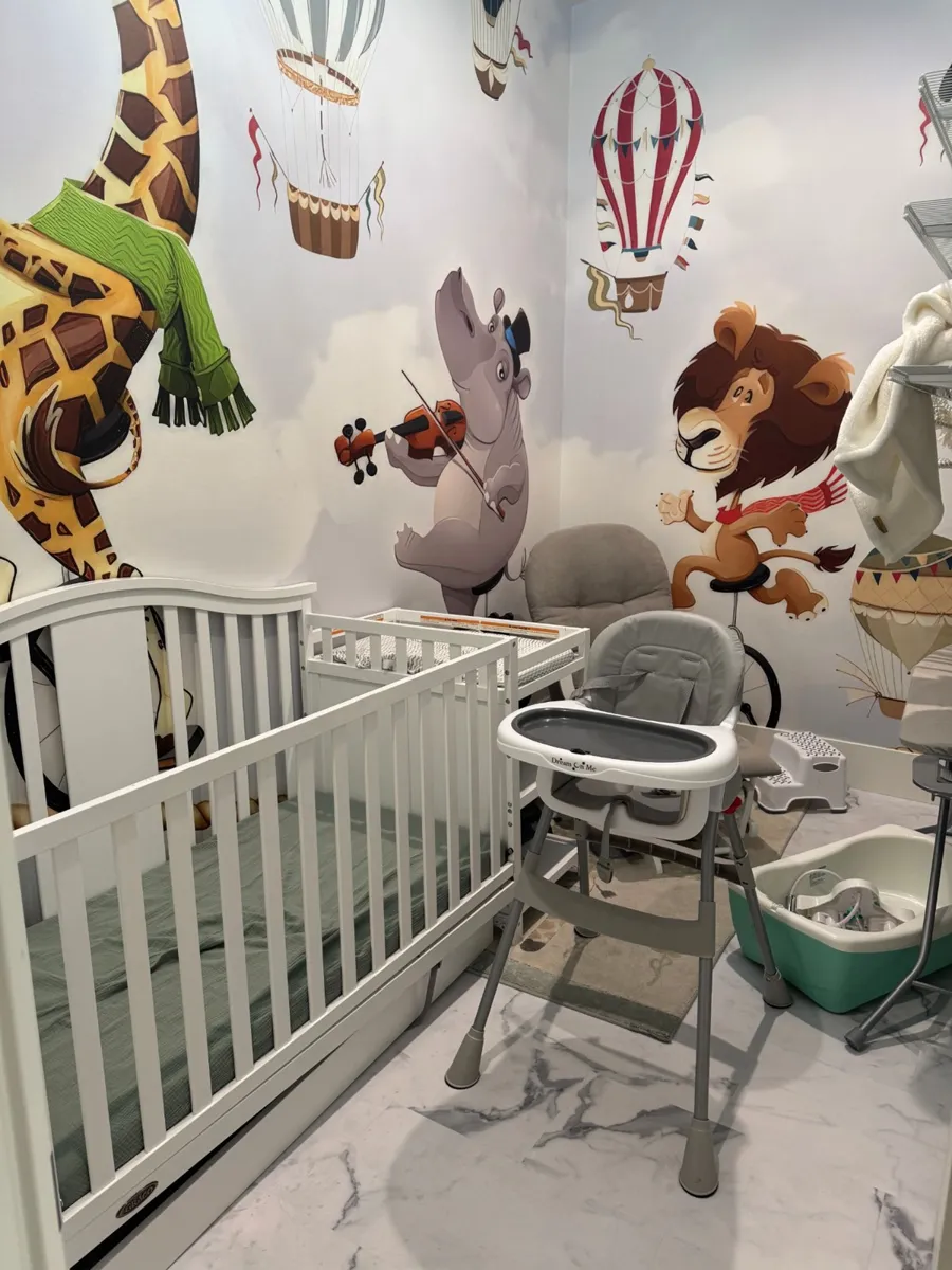 Nursery inside the master suite with a white crib, changing table, high chair, infant bathtub, and a mural of animals and hot air balloons