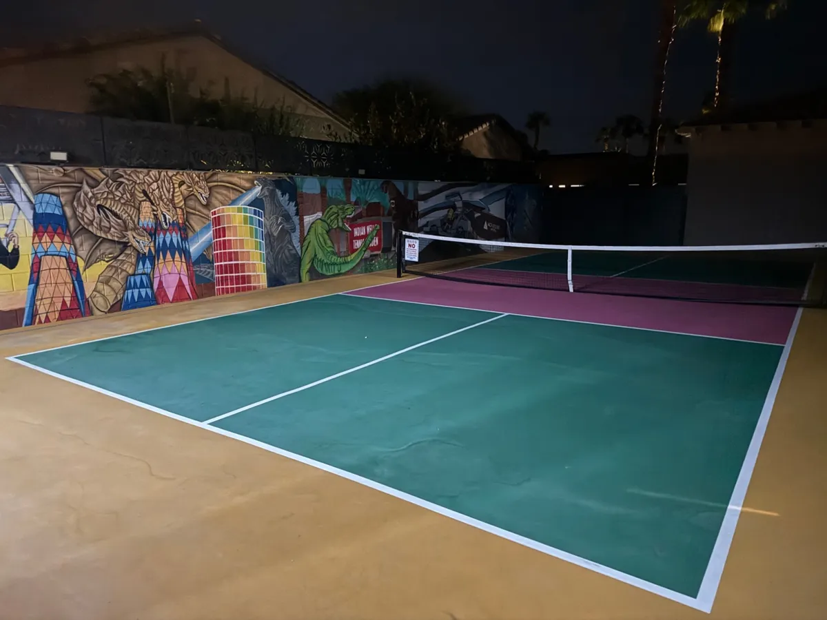 Backyard pickleball court with green and pink surface next to a colorful mural wall