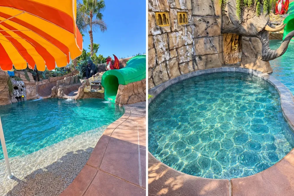 Daytime view of the pool with rock slides and a green tube slide on the left, and the hot tub next to a rock wall with an elephant sculpture on the right