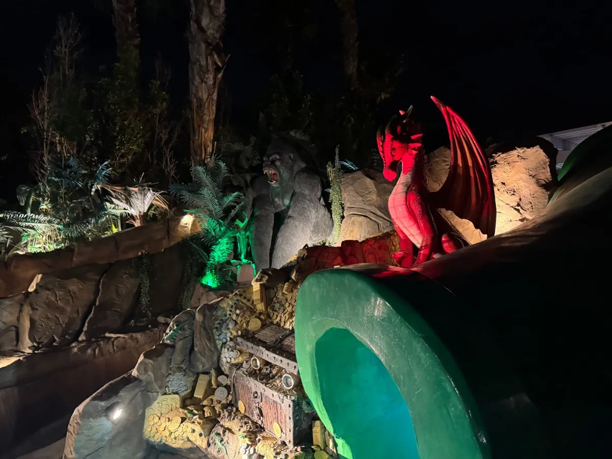 Gorilla and red dragon statues above a treasure chest next to the green tube slide, lit up at night