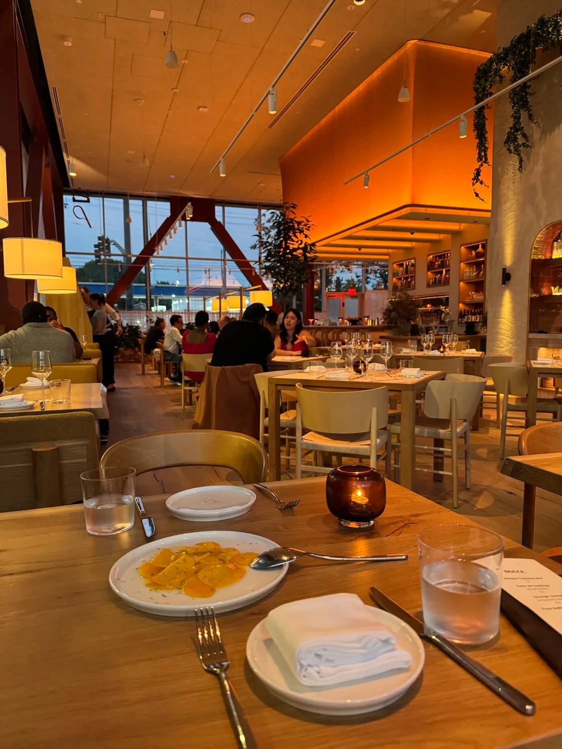 The shaved mango with smoked bone marrow and Santa Barbara uni at Picala, with the warm, candle-lit dining room and open kitchen behind it at dusk