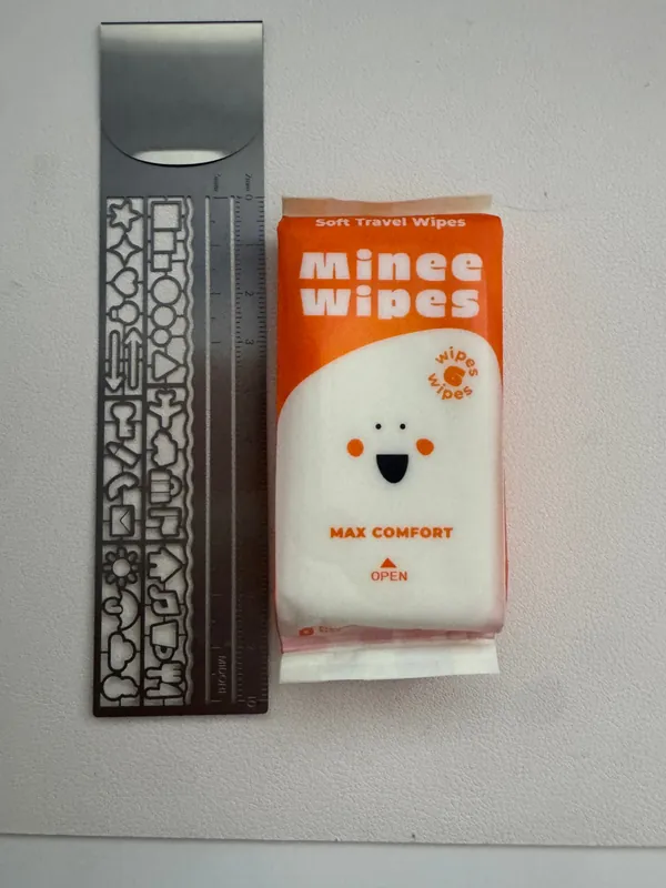 A pocket pack of Minee soft travel wipes next to a 10 cm metal ruler for size