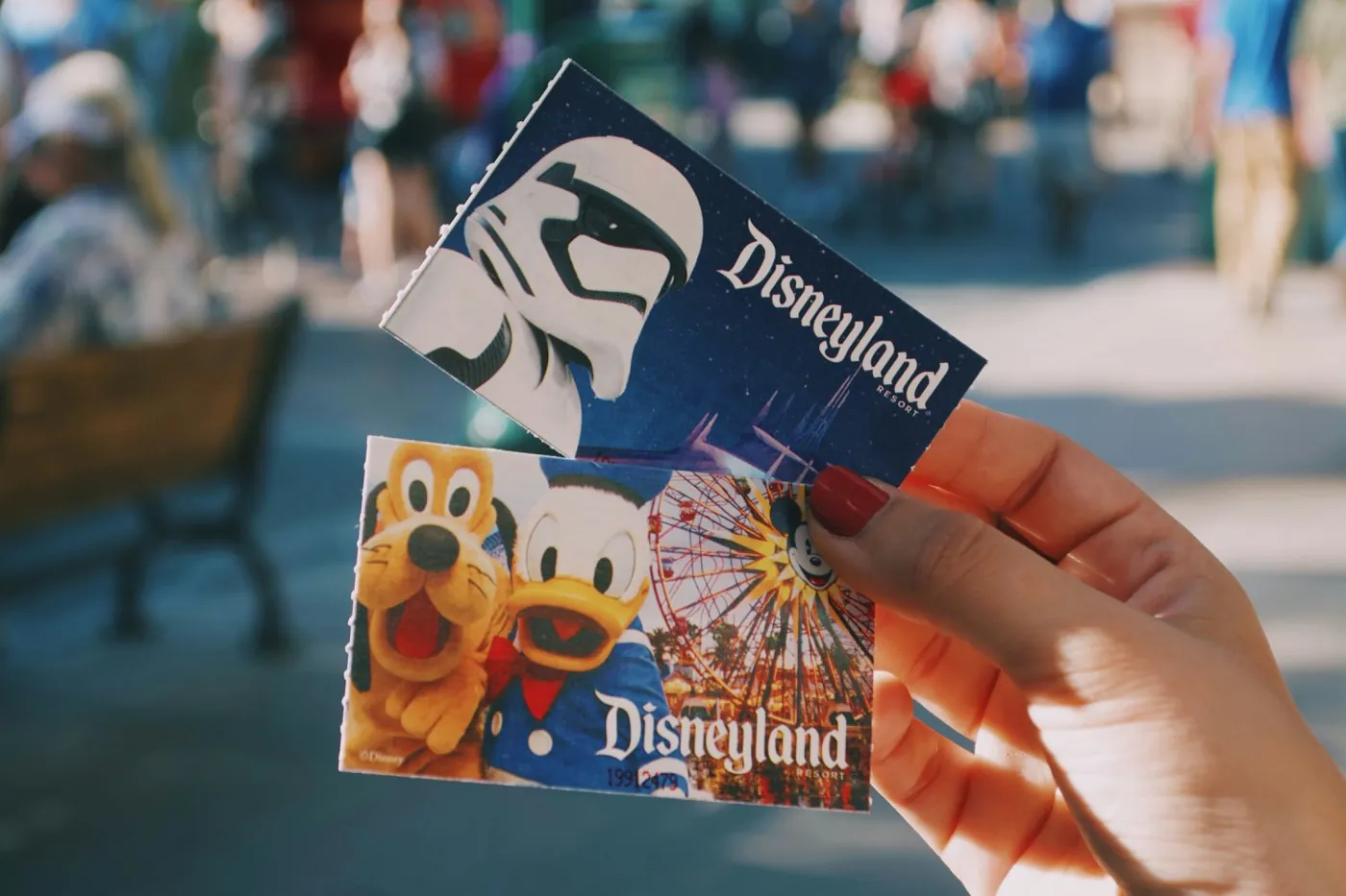 A hand holding two paper Disneyland admission tickets