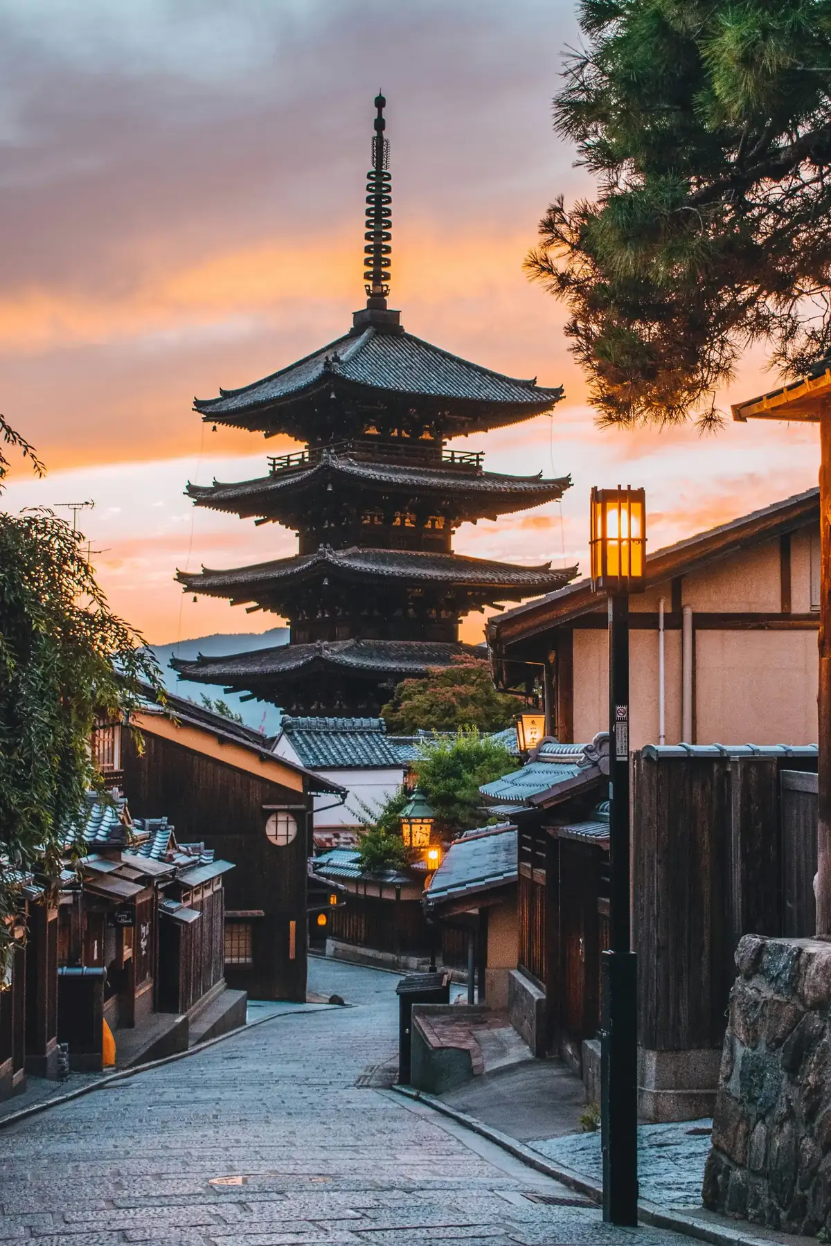 The stone-paved Sannenzaka approach lane, machiya storefronts and a kimono walker at golden hour.